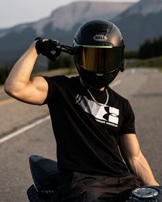 a man riding on the back of a motorcycle wearing a helmet and holding his hand up to his head