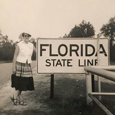 a woman standing next to a sign that says florida state line in black and white