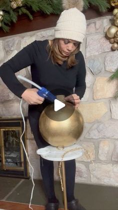 a woman holding a large golden bell on top of a table next to a fireplace