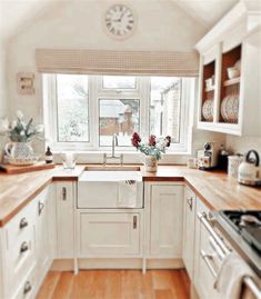 a kitchen with white cabinets and wooden counter tops next to a large window that has a clock on the wall