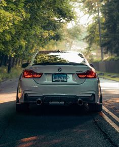 the back end of a white bmw car driving down a road with trees in the background