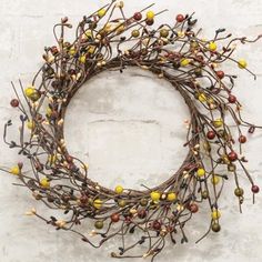 a wreath with yellow and red berries hanging on a white brick wall in front of a window