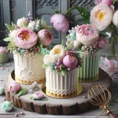 three cakes decorated with flowers on top of a wooden table next to pink roses and other decorations