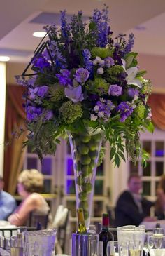 a vase filled with lots of purple flowers on top of a table next to wine glasses