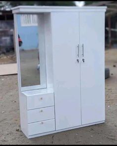 a white armoire sitting on top of a pile of dirt next to a building