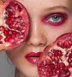 a woman with red makeup and pomegranates on her face is holding up two halves of the pomegranate