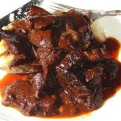 a white plate topped with meat and gravy next to a knife and fork