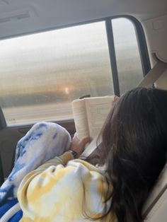 a woman laying in the back seat of a car reading a book