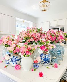 pink flowers in blue and white vases on a kitchen countertop, with an ornate chandelier above