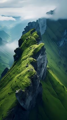 an aerial view of a green mountain with clouds in the sky and grass growing on it