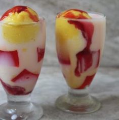 two glasses filled with dessert sitting on top of a marble counter next to each other