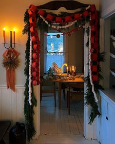 a dining room decorated for christmas with red and white garland on the door, candles in the background