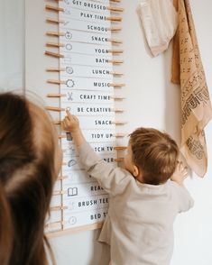 a little boy playing with clothes pegs on the wall in front of a woman