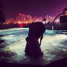 a person sitting in an outdoor hot tub with city lights in the background at night