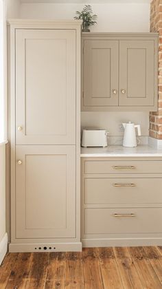 an empty kitchen with white cabinets and wood flooring, in front of a brick wall