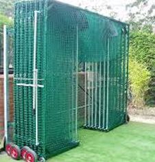 a large green metal cage next to a brick wall and grass area with red wheels