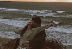 a man and woman sitting on top of a beach next to the ocean at sunset