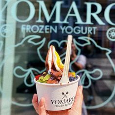 a person holding up a frozen yogurt cup in front of a store window