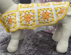 a stuffed dog is wearing a yellow and white crochet blanket on it's back