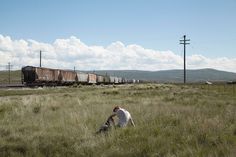 a man kneeling in the grass next to a train