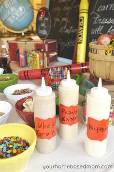 there are three bottles on the table with candy and other items in bowls around them