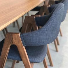 several chairs are lined up at a long wooden table with blue fabric seat covers on it