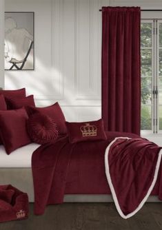 a bed with red comforters and pillows in a white room next to a window