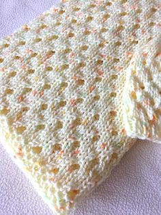 a crocheted blanket laying on top of a white sheet with multicolored dots