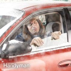 a woman sitting in the passenger seat of a red car with snow all over her