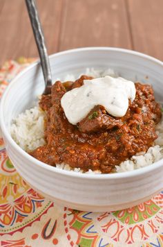 a white bowl filled with rice and meat covered in sauce on top of a colorful table cloth