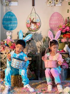 two children dressed up in bunny ears sitting on the ground with easter decorations behind them