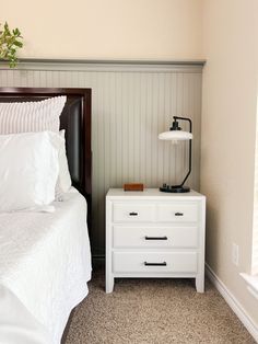 a white bed sitting next to a night stand on top of a wooden dresser under a window