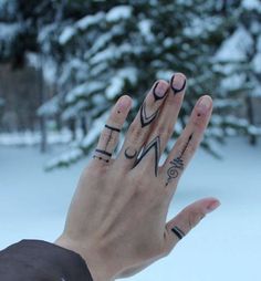 a person's hand with tattoos on it and two fingers in front of snow covered trees