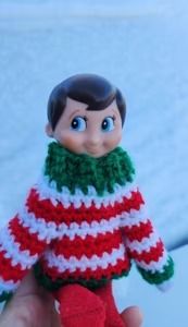 a hand holding a small knitted doll wearing a red, white and green sweater