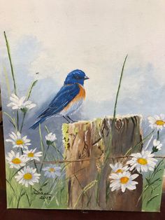 a painting of a blue bird sitting on top of a piece of wood with daisies