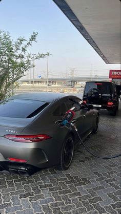 a gray sports car being charged at a gas station with an electric charger attached to it