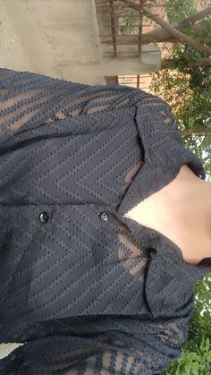 a woman is wearing a black shirt with sheer sleeves and has her hands in her pockets