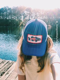 a girl wearing a blue hat with a fish patch on it's side and trees in the background