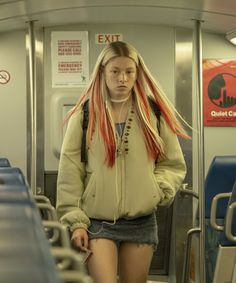 a girl with red hair standing on a subway train looking at the camera and listening to headphones