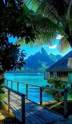 a wooden walkway leading to a beach with mountains in the background and blue water on both sides