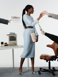 a woman standing in front of a desk with a computer chair and other people around her