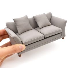 a hand holding a miniature couch with four pillows