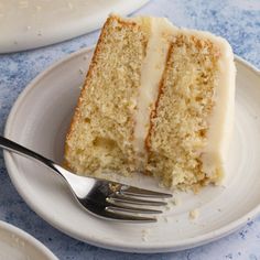 a slice of cake on a white plate with a fork next to it and another piece in the background