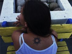 a woman sitting on a bench with her back turned to the camera and sun tattoo on her upper arm