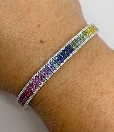 "Stunning Rainbow Sapphire Bracelet White Gold.  Excellent craftsmanship, excellent quality multicolor sapphire gems.  The colors are rich and vibrant, full of life.  All princess cut and are diamond cut gems, so each gem sparkles beautifully.   Nice and smooth setting, lays perfectly on the wrist. Bracelet measures just shy of 7\".  The width is about 7.6mm width.  Two side safety latches for a secure fit. The diamonds are very sparkling.  Give the gift of this lucky rainbow bracelet that will be treasured for a lifetime.   Genuine earth mined fancy color sapphires total weight: 13.43 carats All princess cuts  Clean and vibrant gems  Invisible Setting Genuine earth mined round brilliant cut diamonds total weight: 1.87 carats Clarity: SI Color: F Solid 18K White Gold 18.19 grams Comes with Tennis Bracelet Colored Stones, Gemstone Tennis Bracelet, Rainbow Sapphire Bracelet, Rainbow Tennis Bracelet, All Princess, Sapphire Tennis Bracelet, Bracelet White Gold, Dope Jewelry Accessories, Multicolor Bracelet