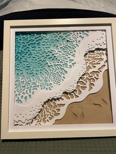 an intricate paper cut artwork depicting the beach and ocean waves in blue, beige and white