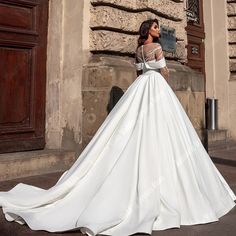 a woman in a white wedding dress is standing on the street and looking at something