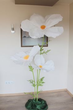 three white flowers in a green vase on the floor next to a framed picture and wall