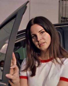 a woman holding her hand up in front of the door of a car and pointing to it