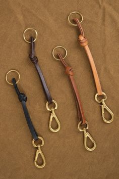 four different types of leather keychains on a brown cloth covered surface with gold metal handles